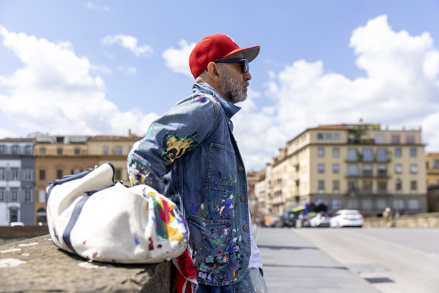 Walking the Lungarno with a white canvas bag, paint-marked denim against the Florence rooftops