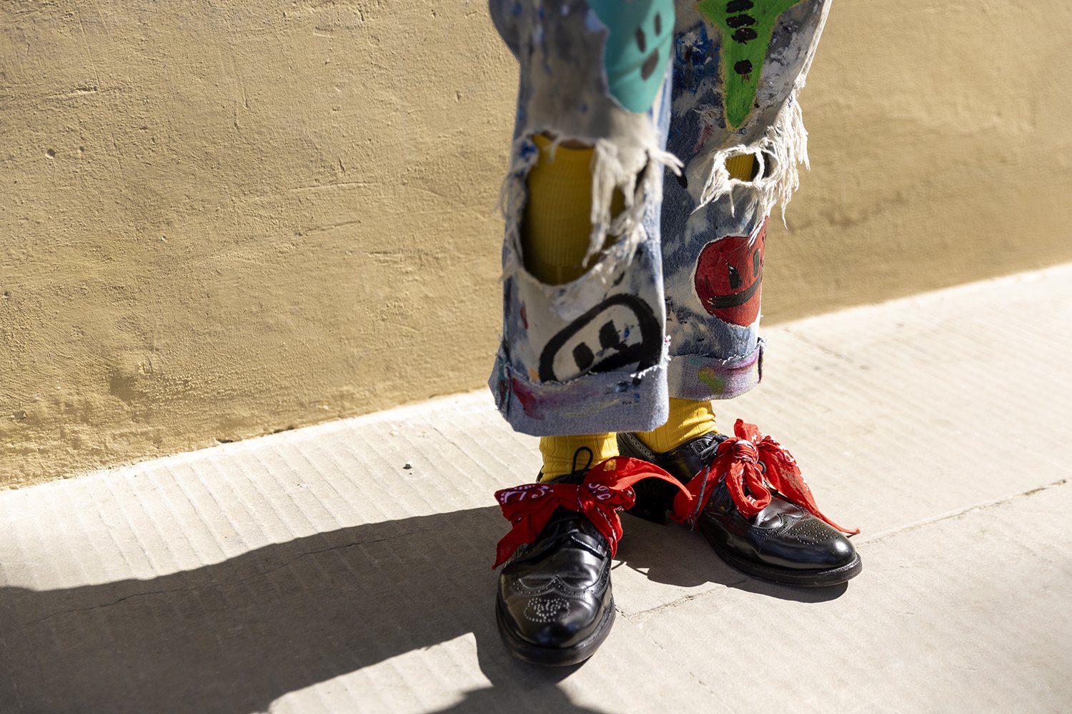 Detail of patched, paint-spattered trousers, yellow socks and black shoes with red laces