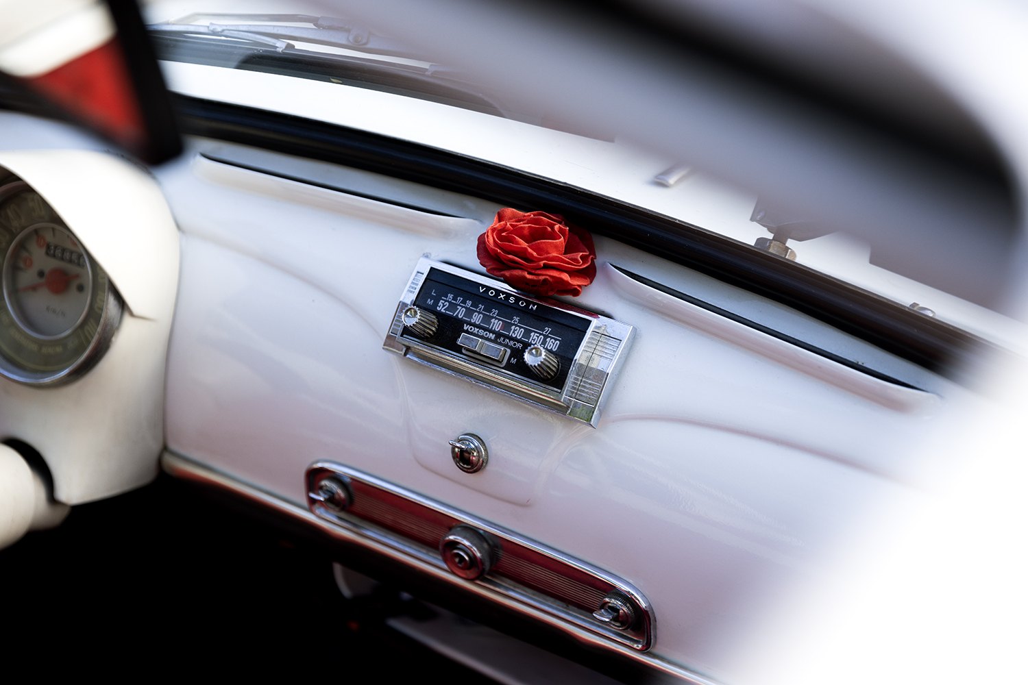 A single red rose tucked beside the radio of a white vintage Fiat 500
