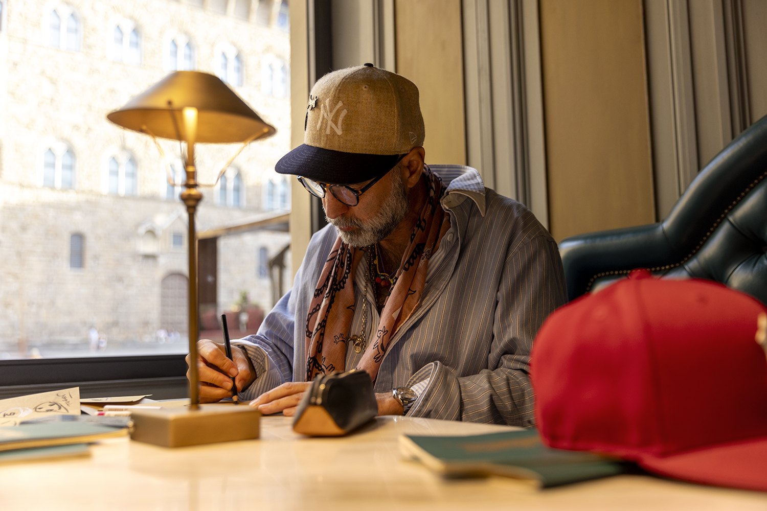 Furia works at a desk by the window, a red cap beside him and Palazzo Vecchio outside