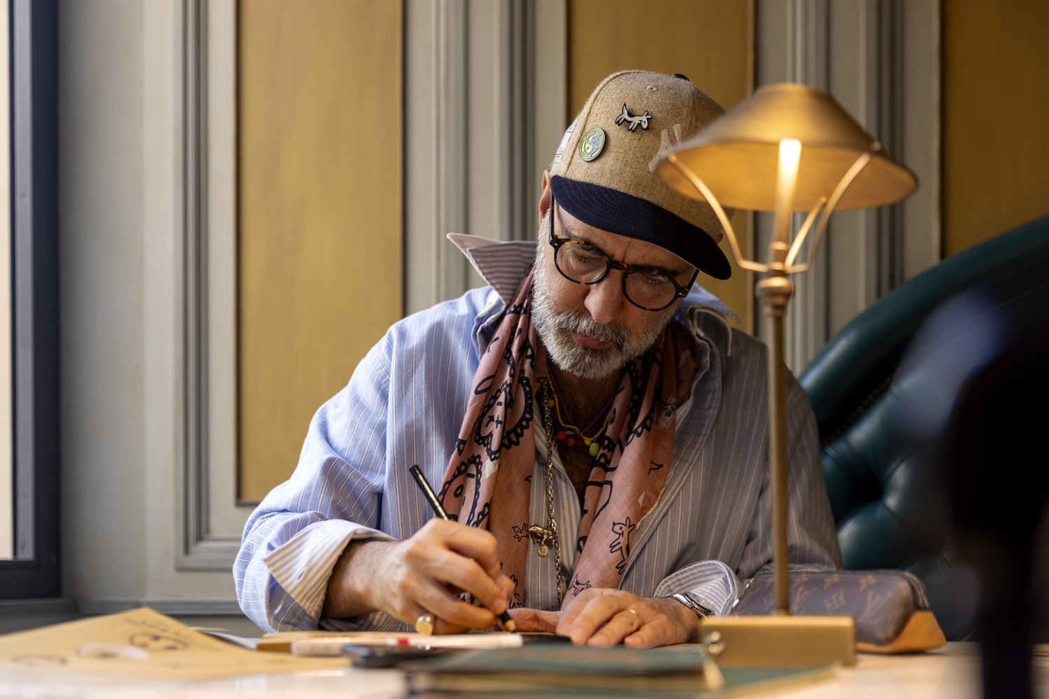Bent over the desk under a brass lamp, brush in hand, glasses down