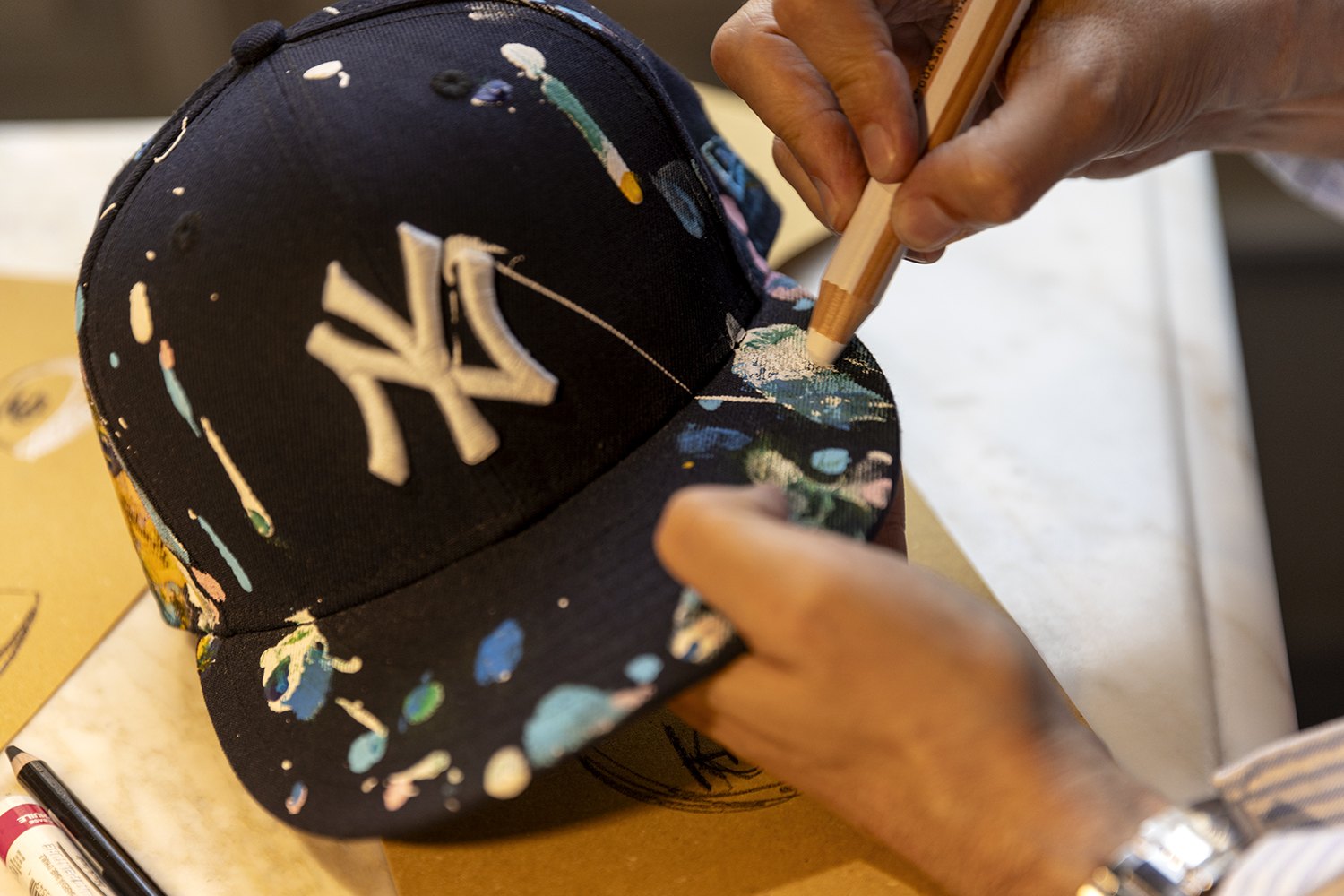 Close-up of a navy New York cap being hand-painted, the brim already flecked with colour
