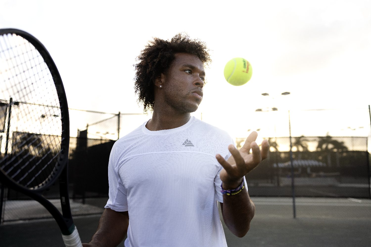 A player tosses a ball to serve, framed by a racket