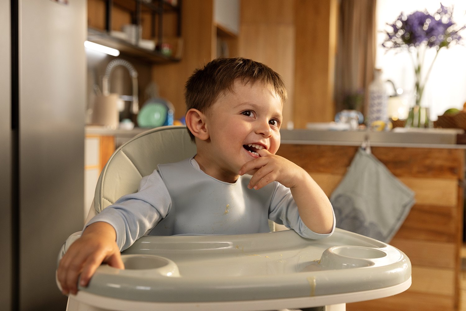 The same child laughing with a hand to his mouth, caught mid-delight in the high chair