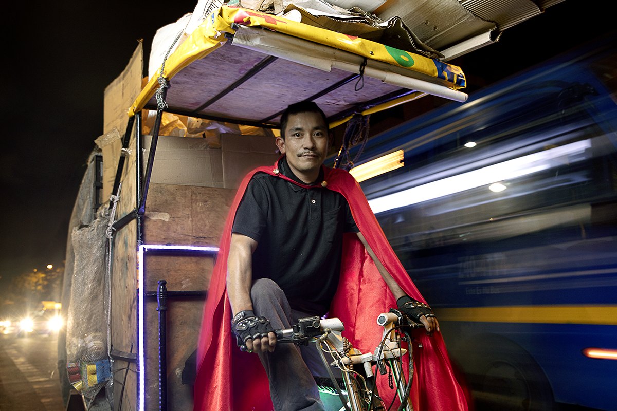 A caped rider on his cart bike as a bus blurs past in the next lane