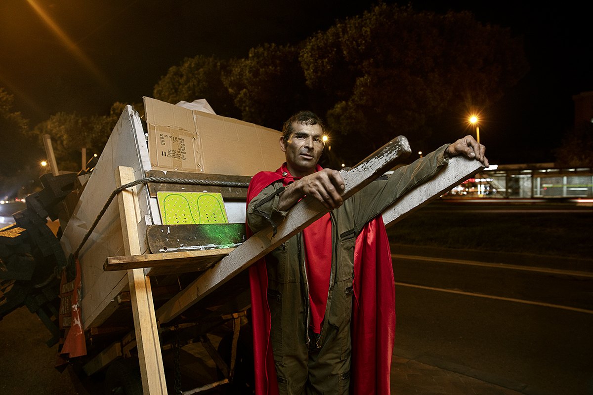Steadying a sheet of flattened board on his cart at the roadside after dark