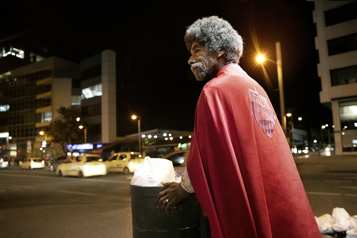 A grey-haired man draped in red turns back towards the lit street