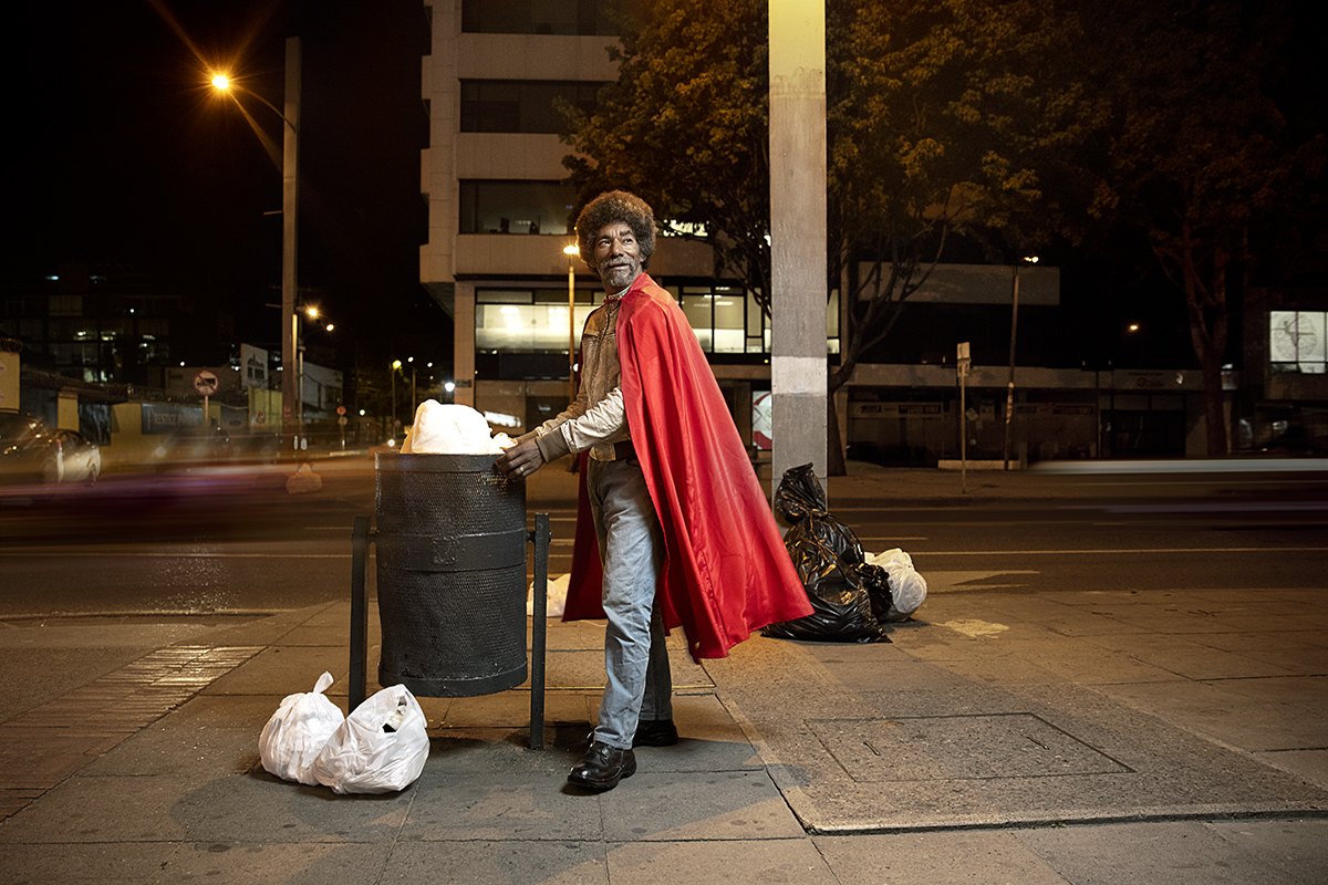 Standing beside a bin and a bundle of bagged recycling under a street lamp