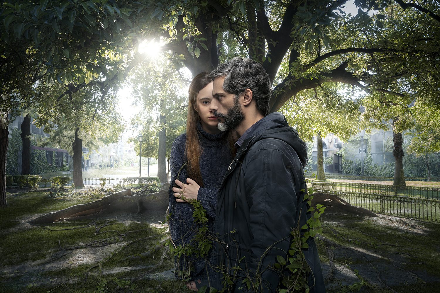 Two figures embrace in a green, overgrown park