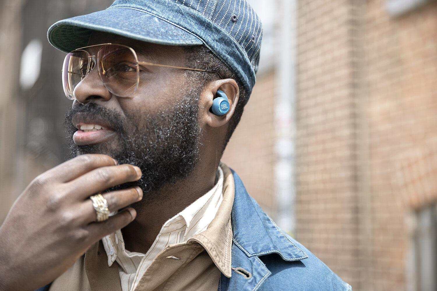 Close portrait in denim cap and glasses, blue JBL earbud catching the light