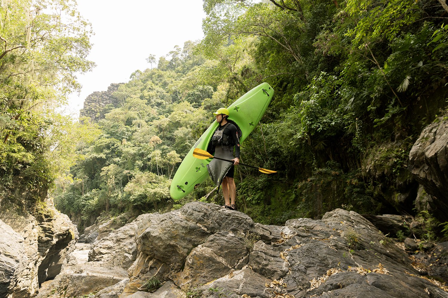 A kayaker stands on a rock, boat raised, canyon behind