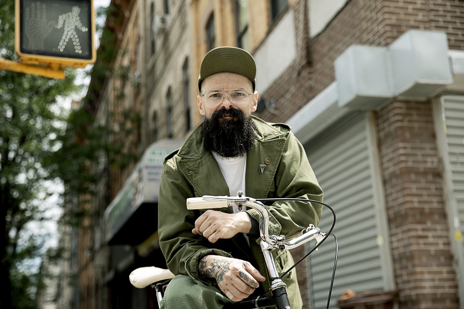 Sitting up on a bicycle outside a shuttered brick storefront, crosswalk signal overhead