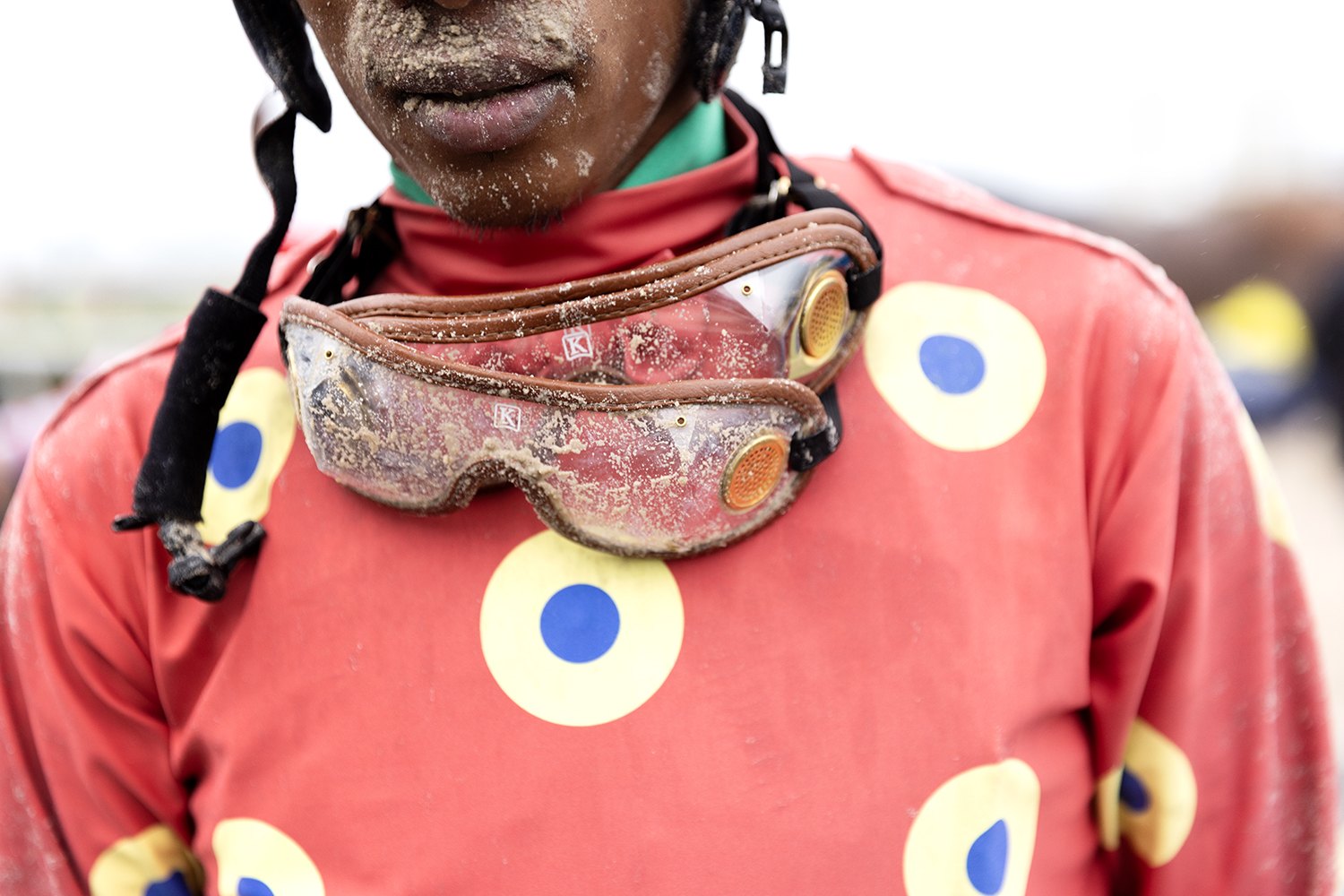 Close detail of mud-packed goggles hanging at the throat of a rider's silks