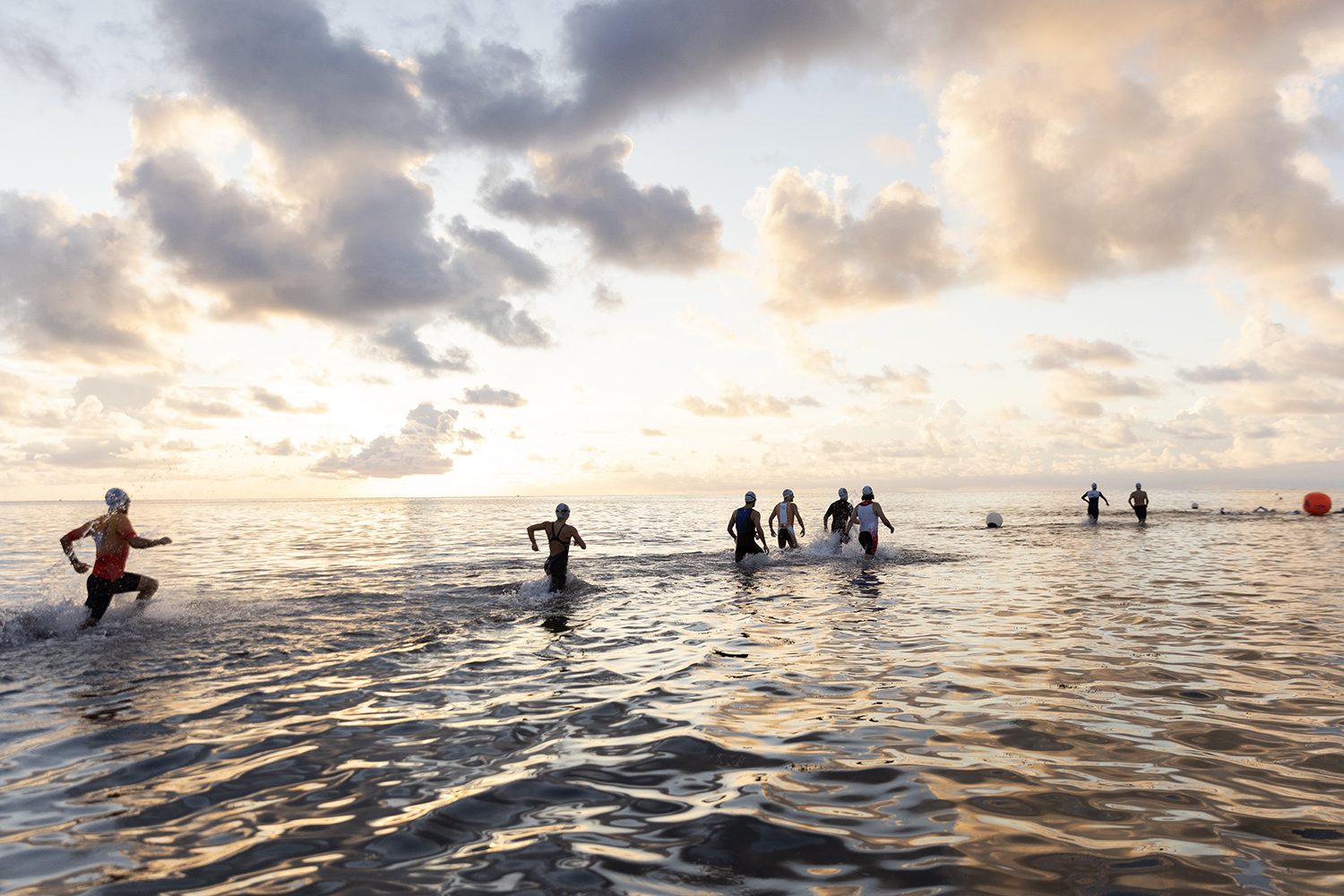 Athletes wade into the calm sea as the sun rises