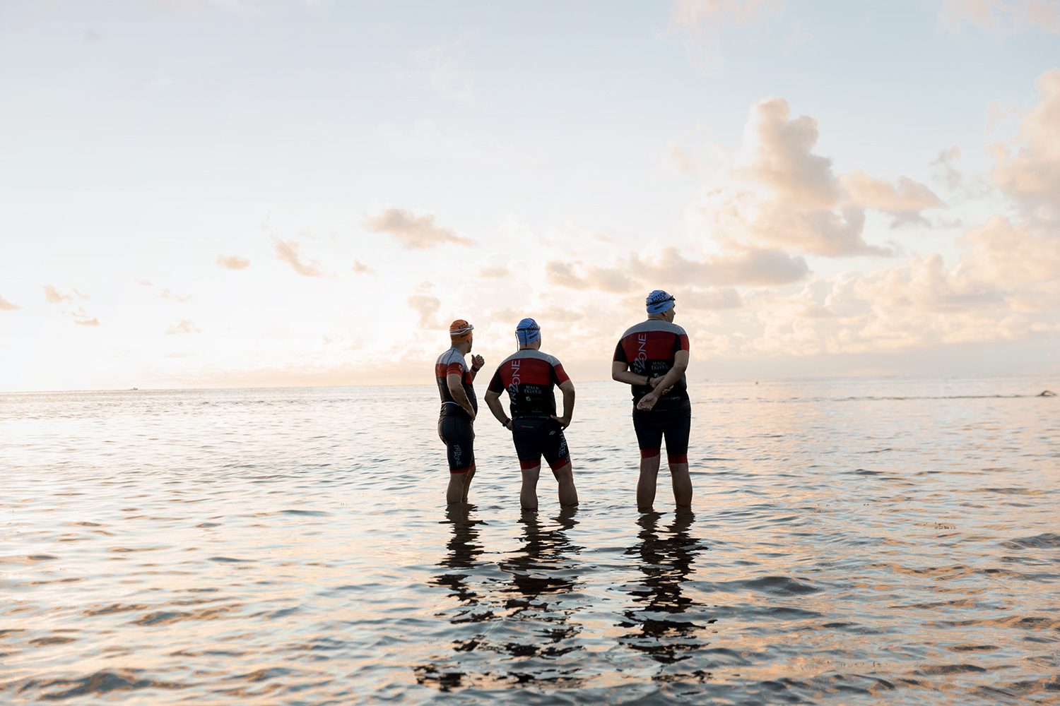 Three triathletes stand in the shallows before the start