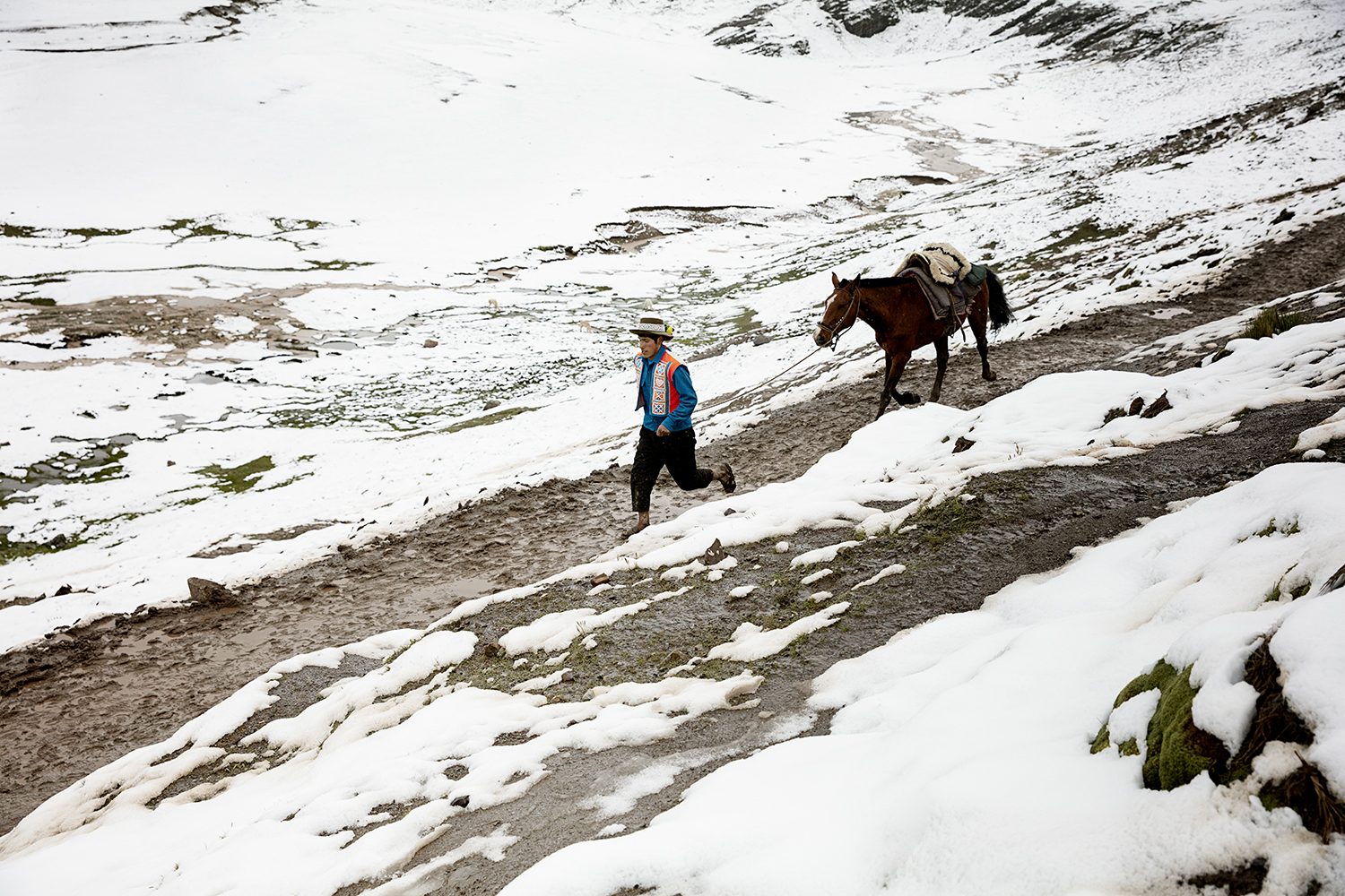 A lone horse and figure cross a vast snowy Andean plain near Vinicunca
