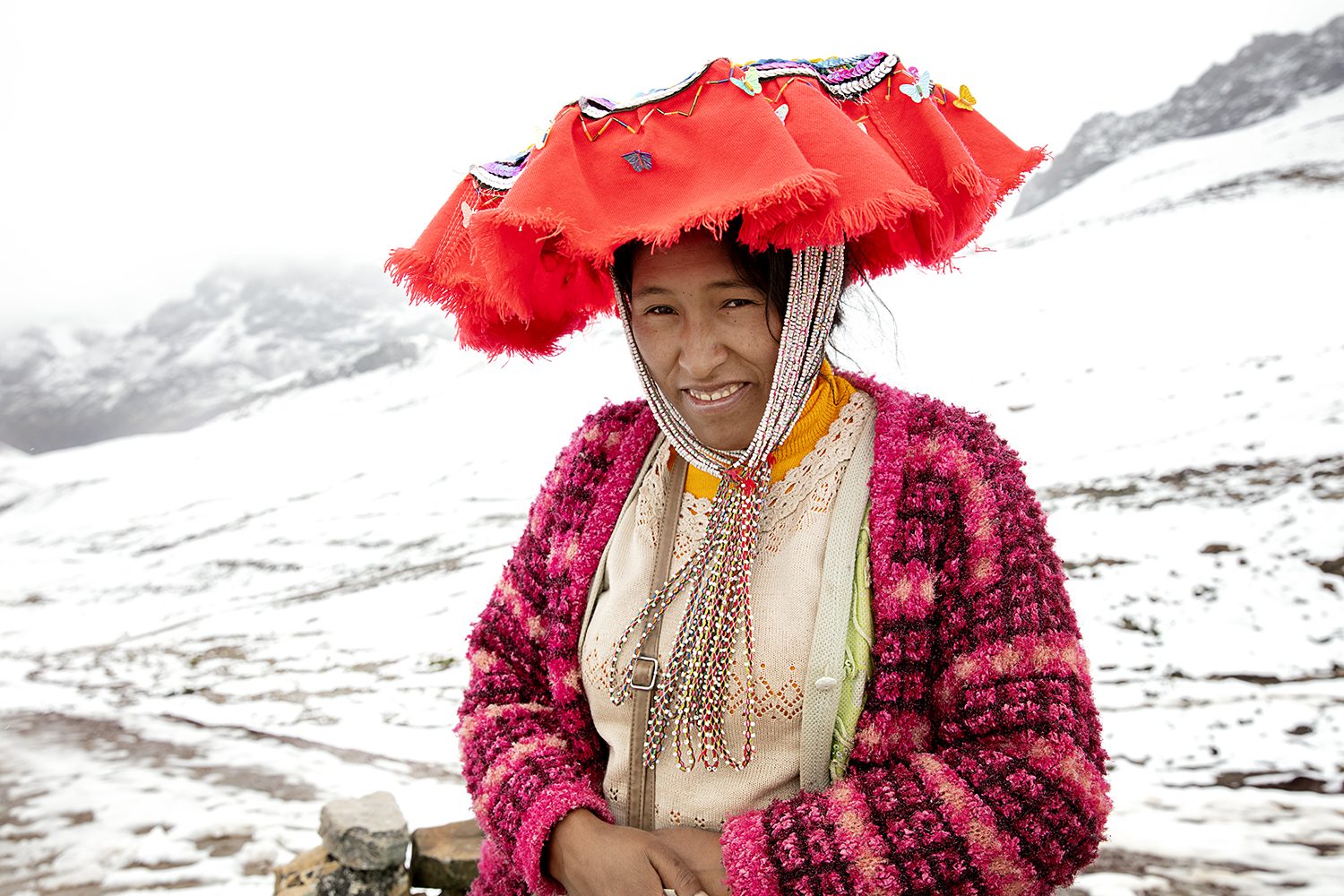 Portrait of a Quechua woman under a red headdress, smiling