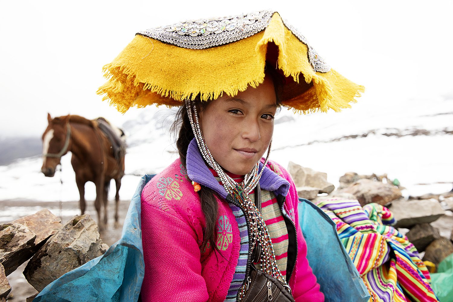 A woman in a yellow montera with her horse in the Andes