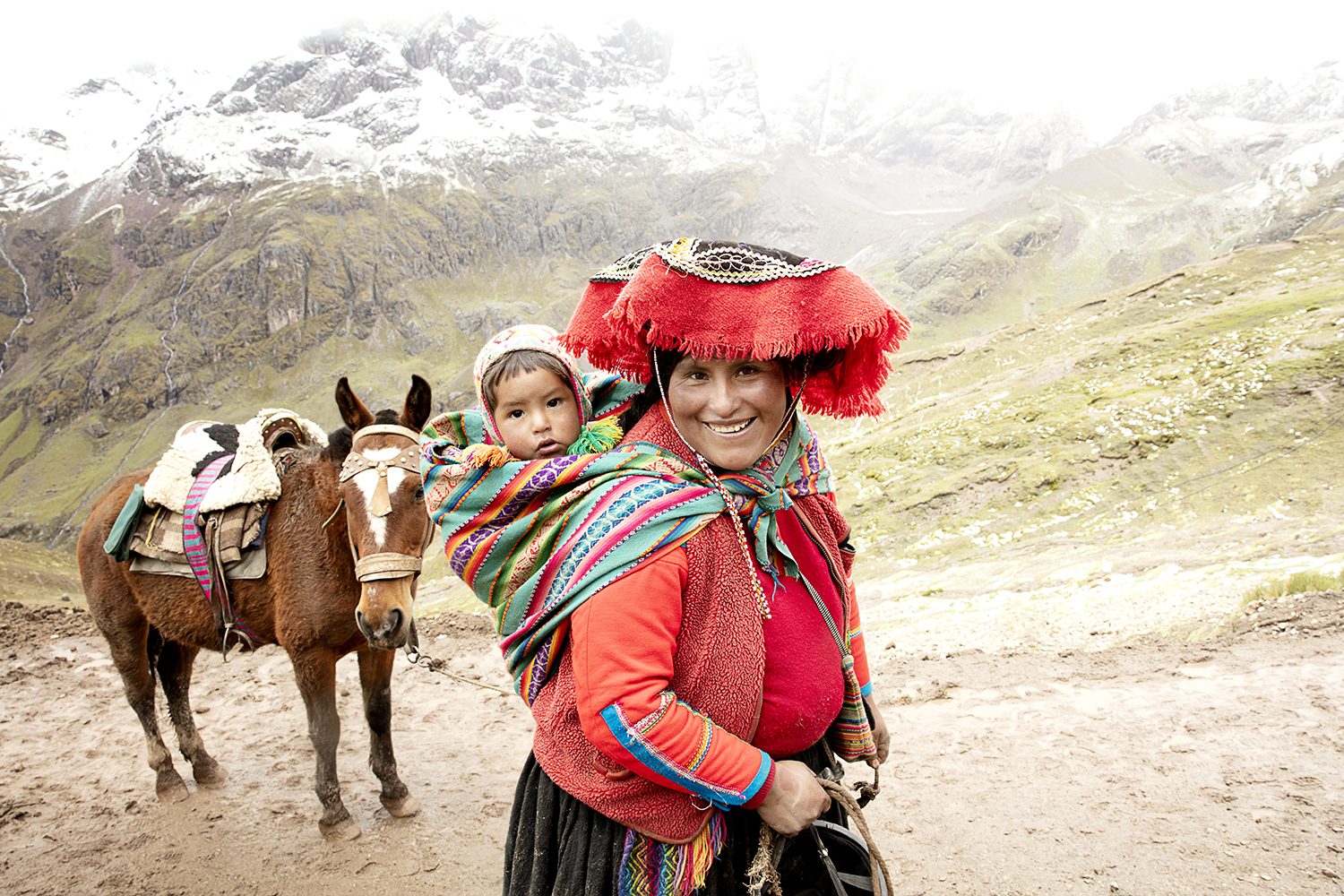 A mother carries her child on her back along the mountain trail
