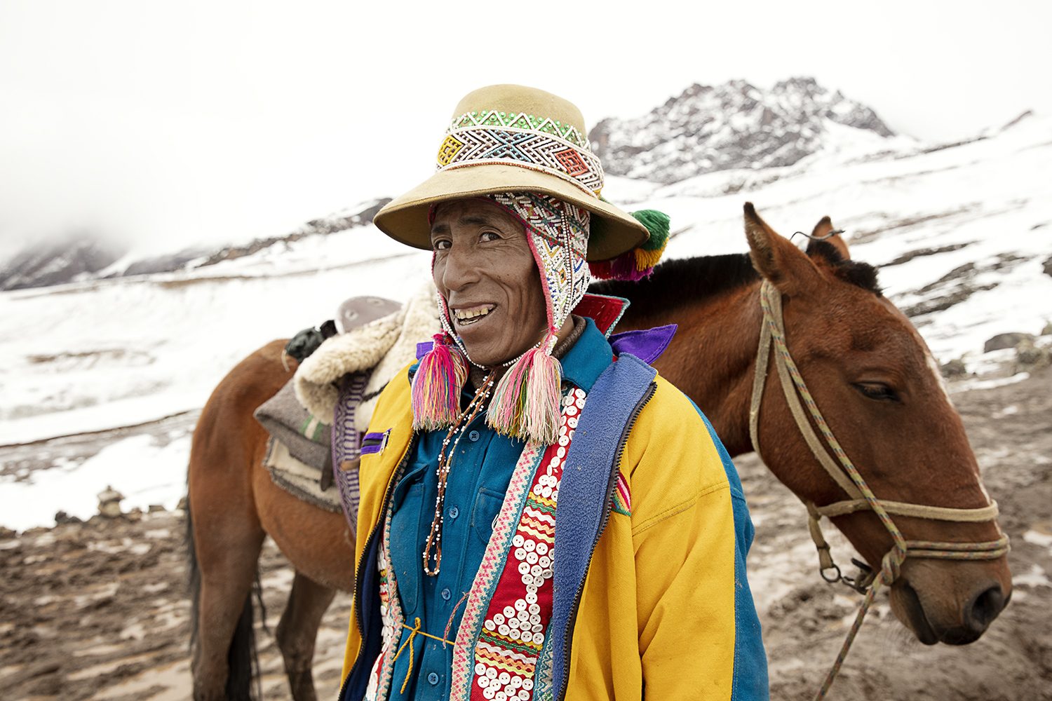 A man in a hat leads his horse, dressed in bright colours