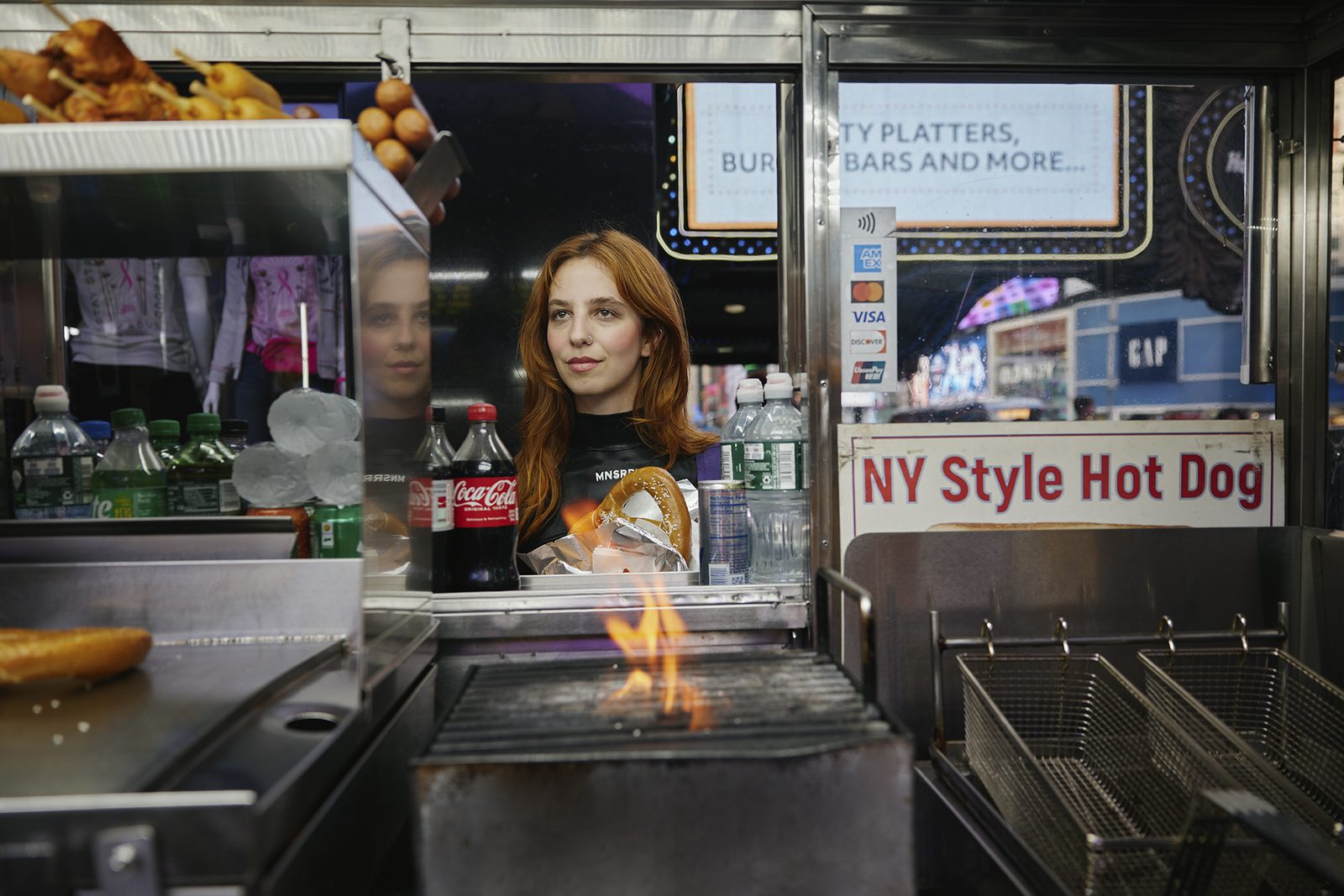 A woman at a glowing hot-dog cart at night
