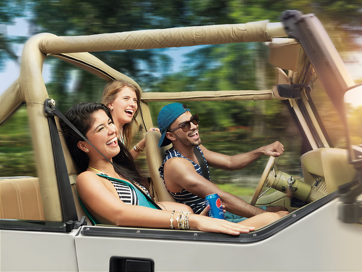 Three friends laughing in an open-top jeep on the way to the beach