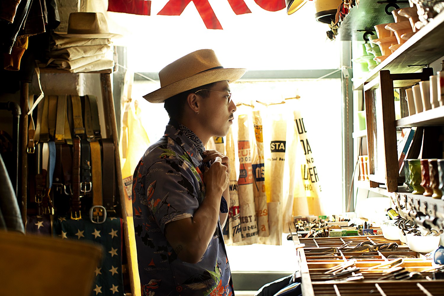 Standing in profile in a narrow aisle lined with hanging belts and leather goods