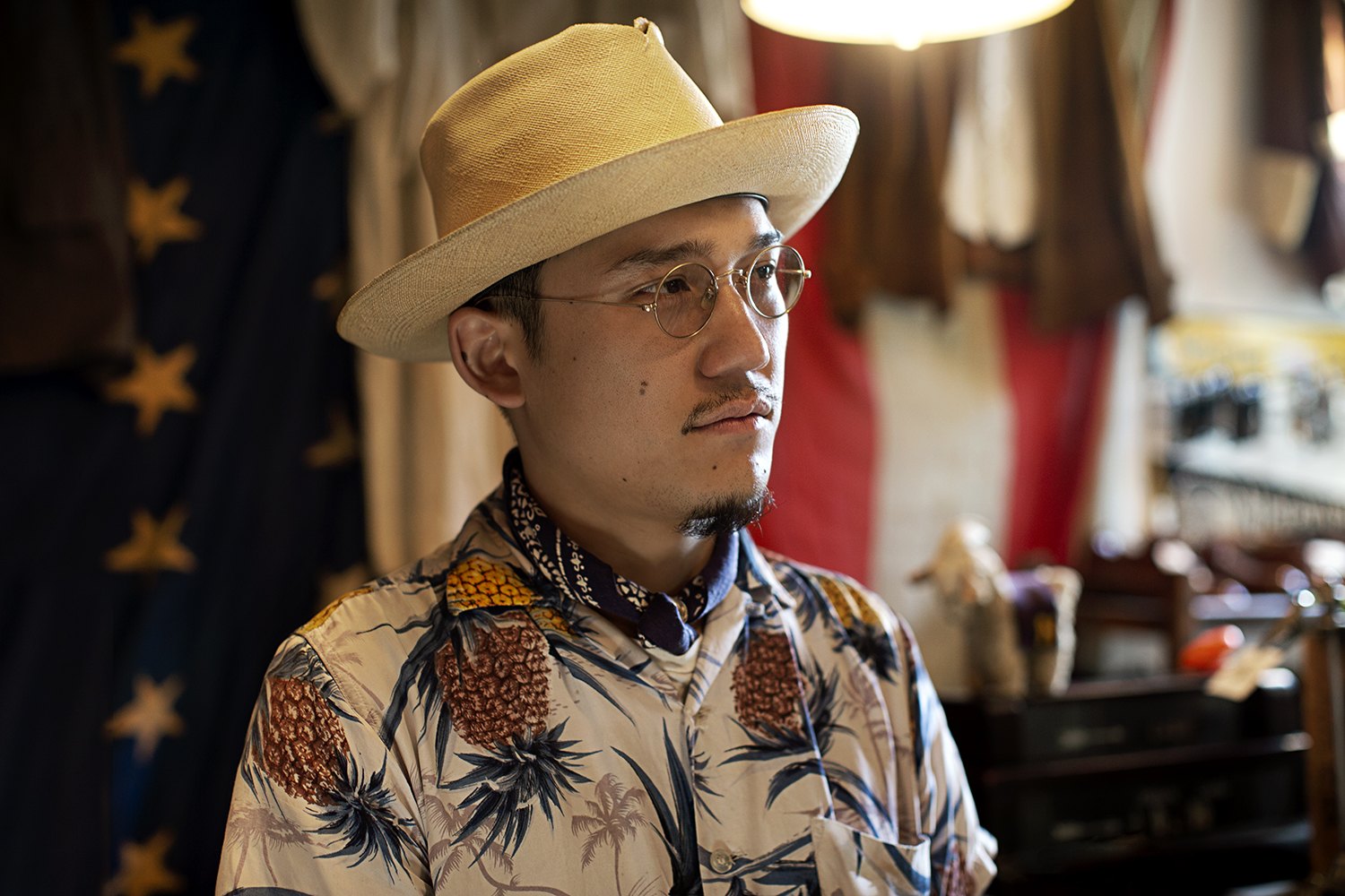 Close portrait under the brim of the straw hat, stall colour soft behind him