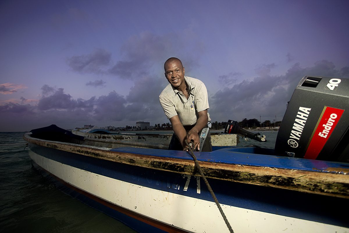 A fisherman leans on his boat with the motor behind him