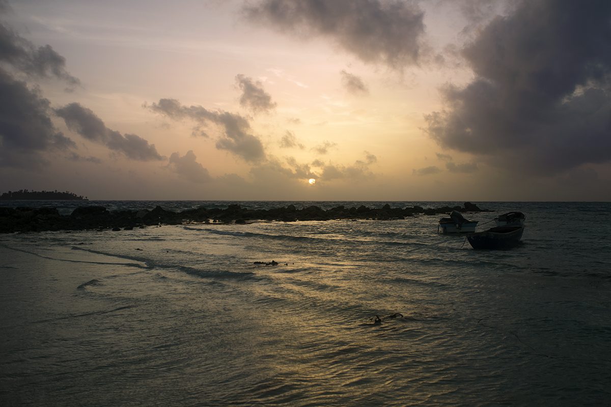 The sun sets over the sea and a moored boat
