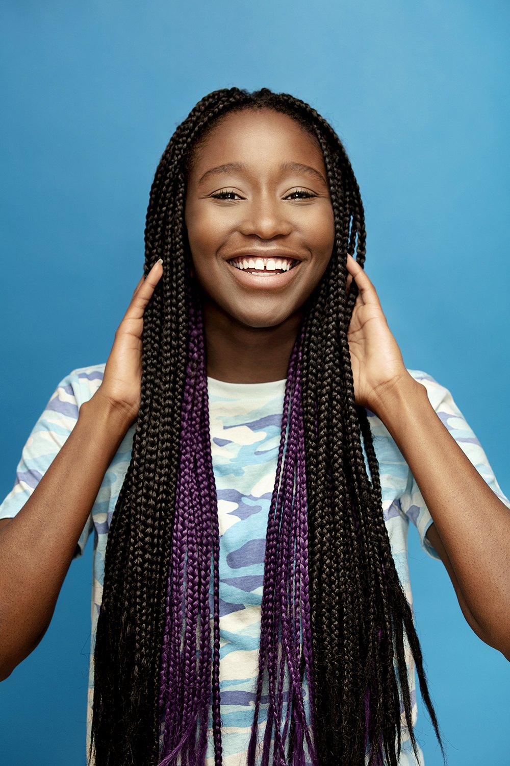 A woman with long braids smiling directly into the lens on blue