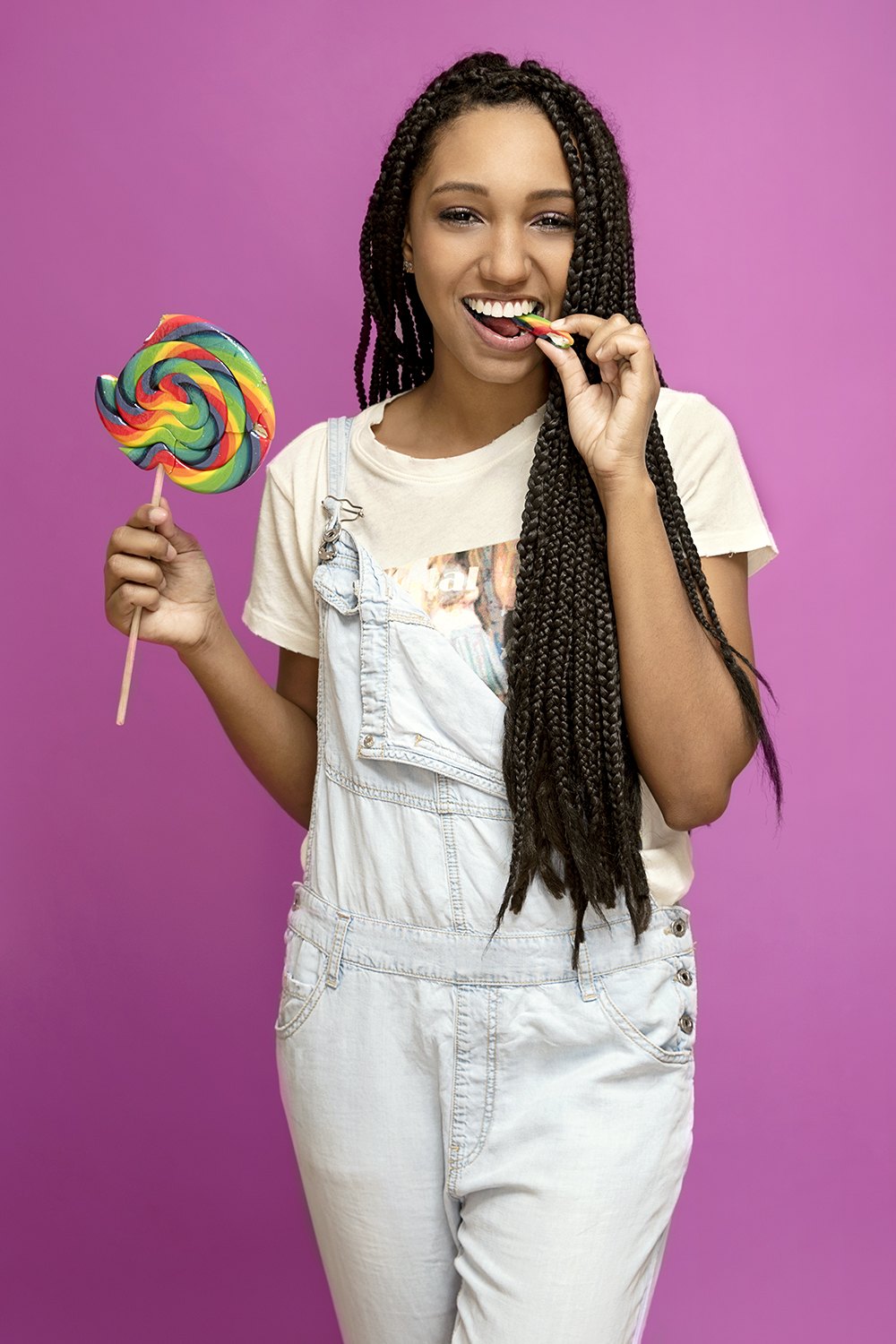 Holding up a spiral lollipop, mid-laugh, magenta backdrop