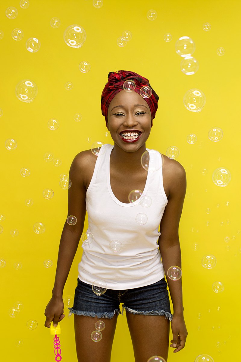 The same subject laughing as soap bubbles drift across the yellow backdrop