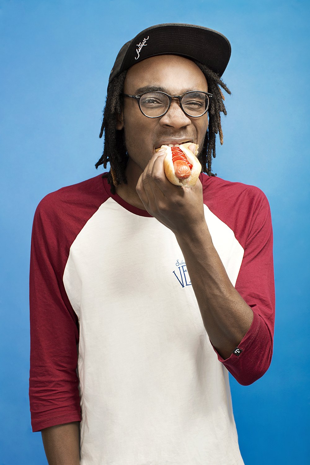 A subject in a raglan shirt eating on set, caught between takes