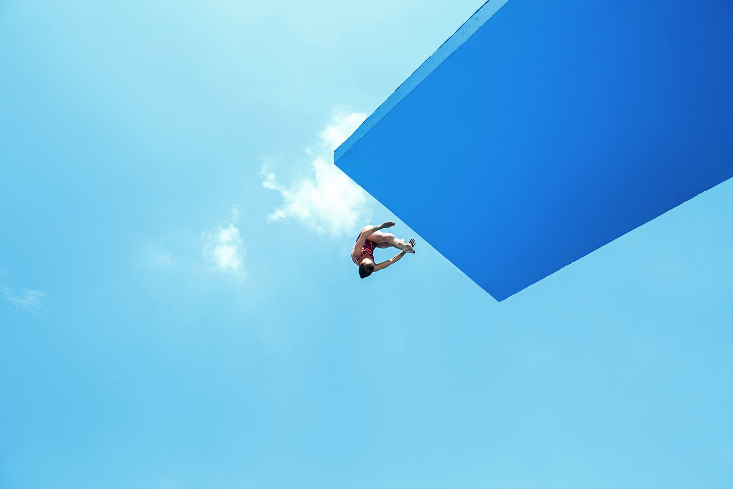 Looking up from the water at a diver stepping off the underside of a blue platform against open sky
