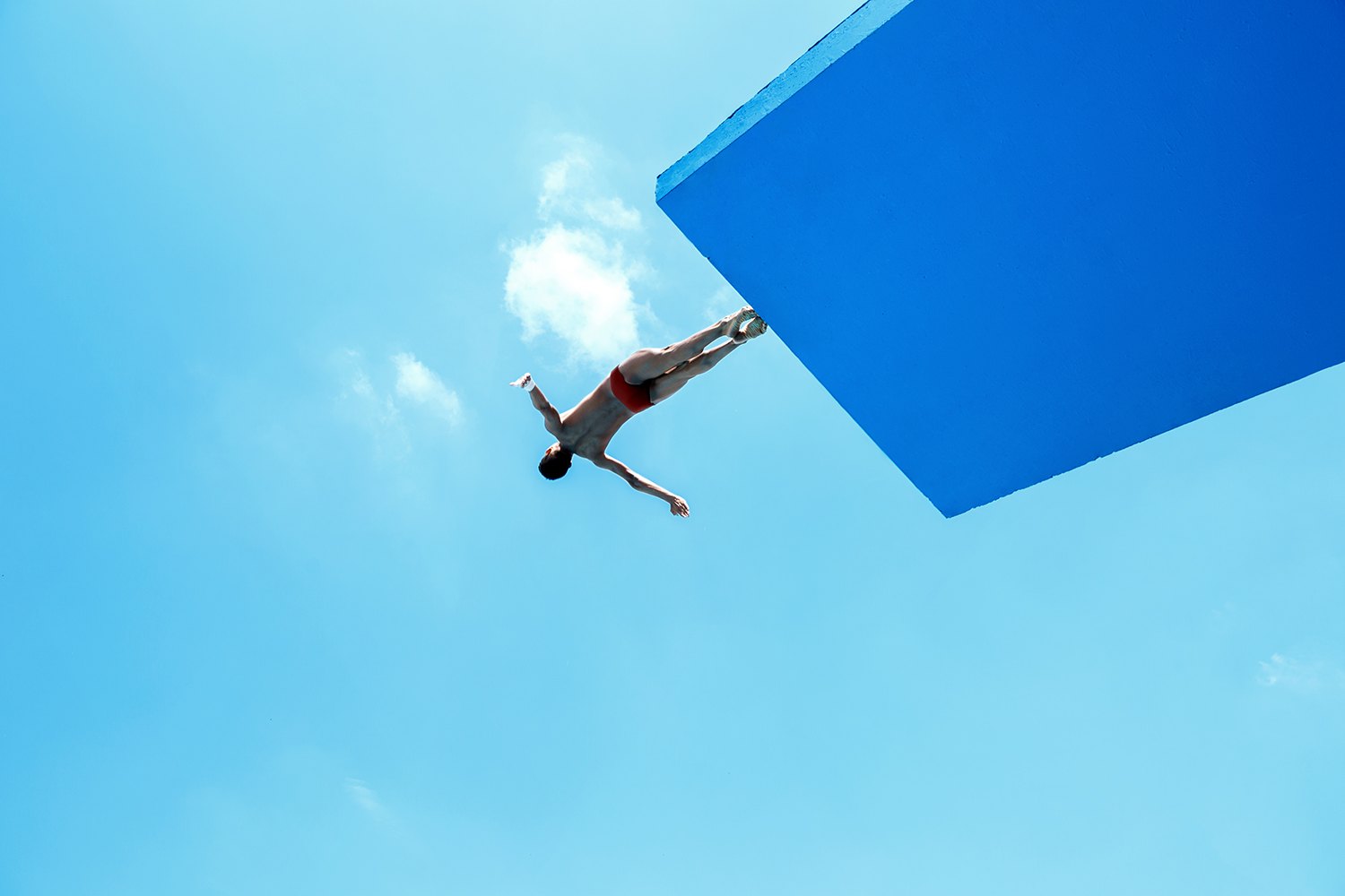 A diver in full extension against blue sky and a single cloud, platform edge cutting the corner