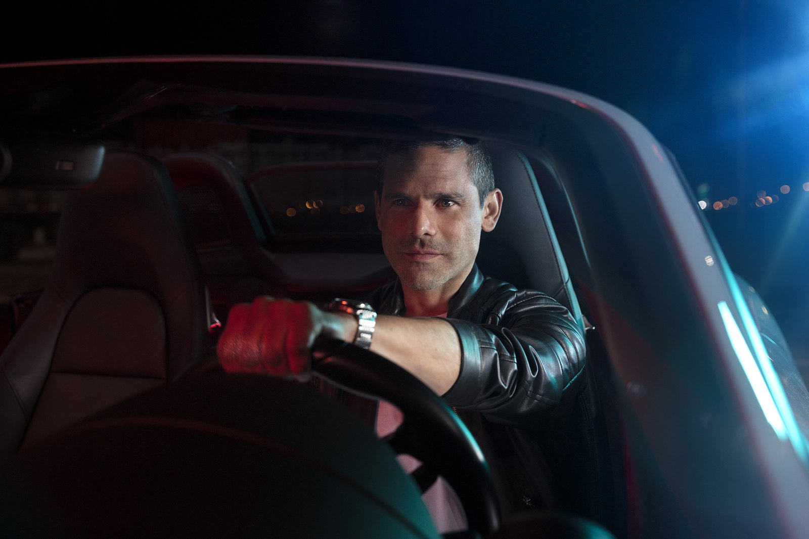 A driver in a leather jacket at the wheel at night, lit only from the dashboard