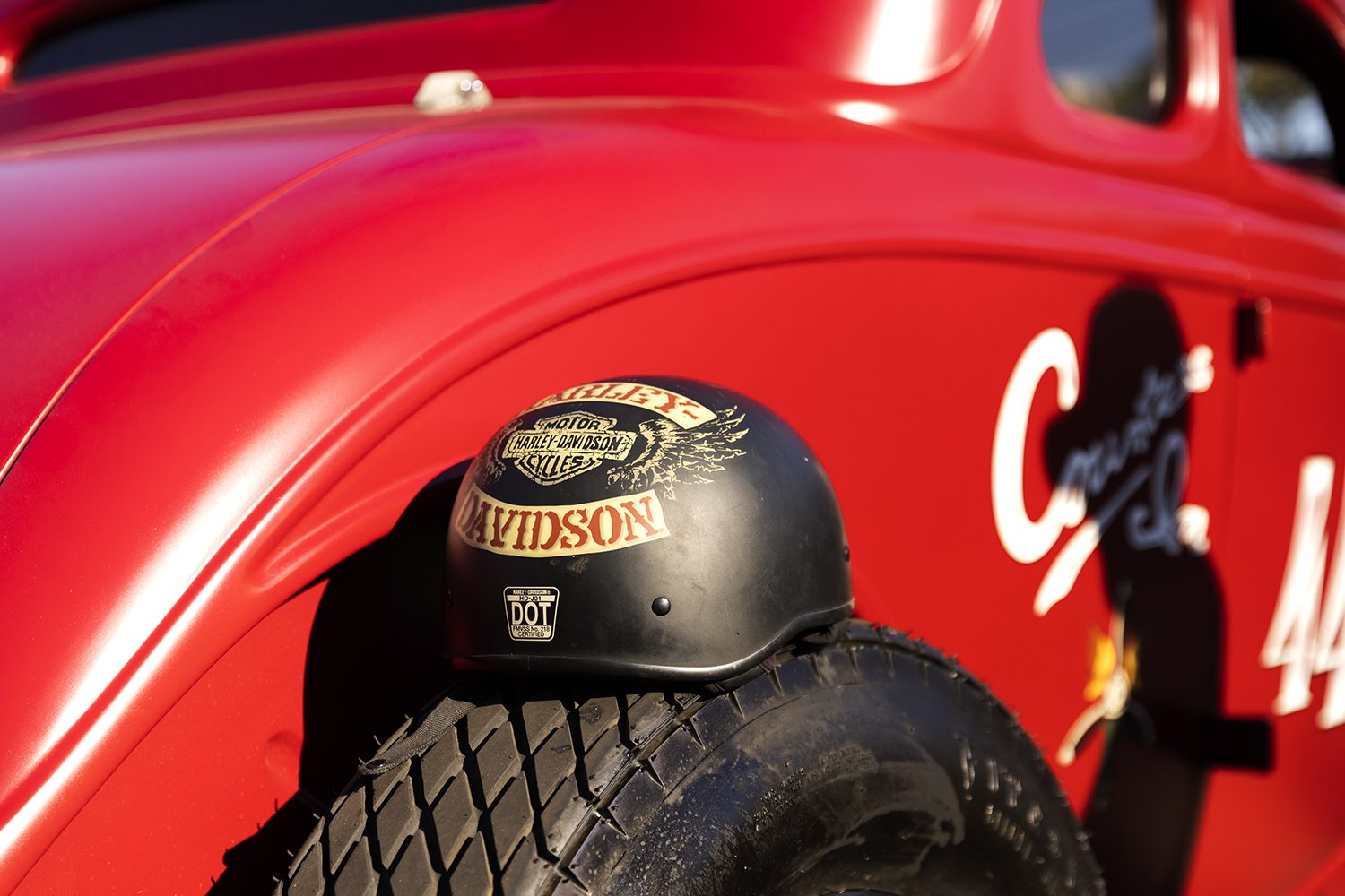 A helmet rests on the tyre of a red hot rod