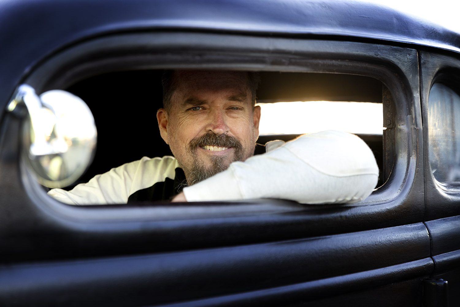 A driver smiles from the window of a black hot rod