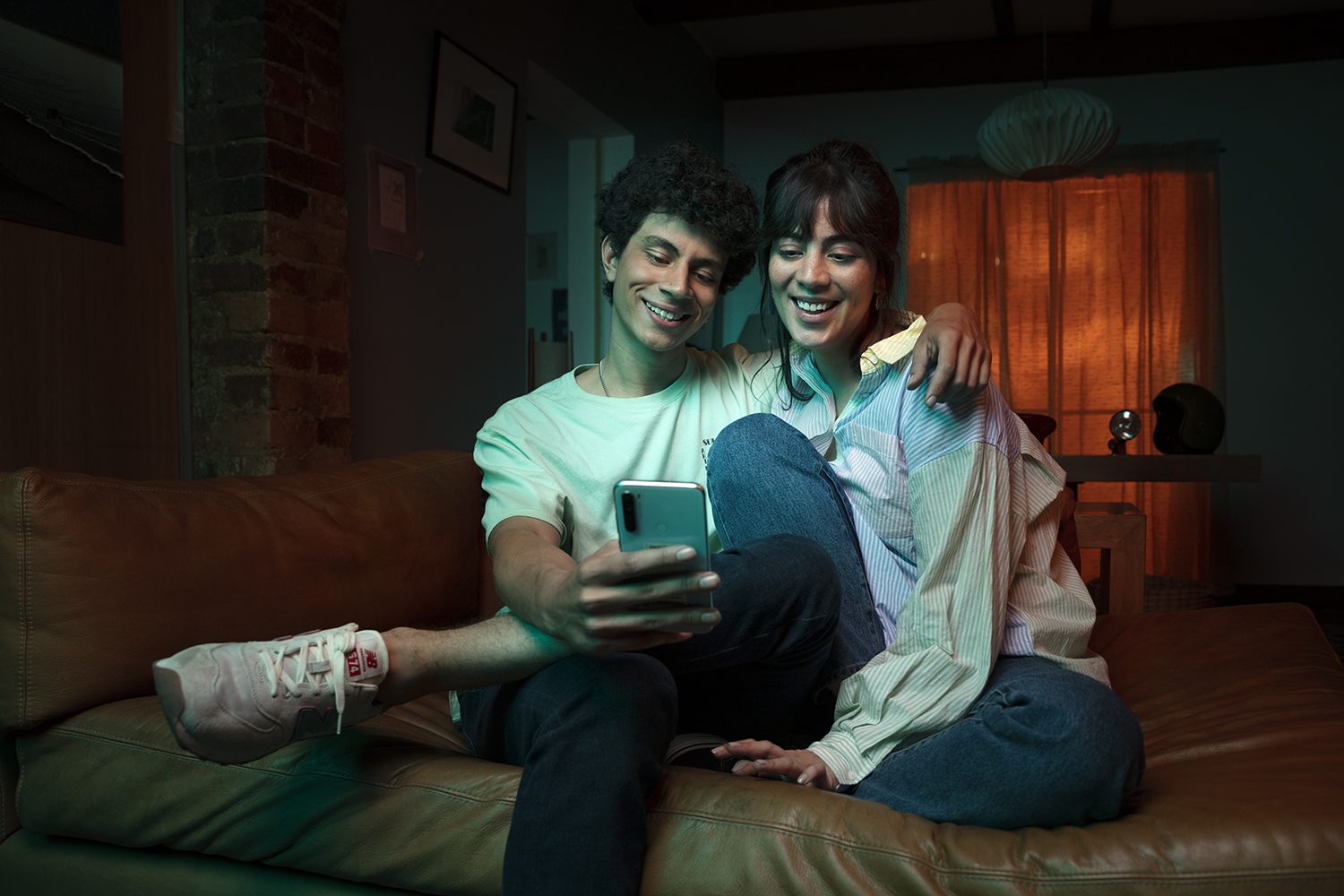 A couple relaxes on a couch checking a phone