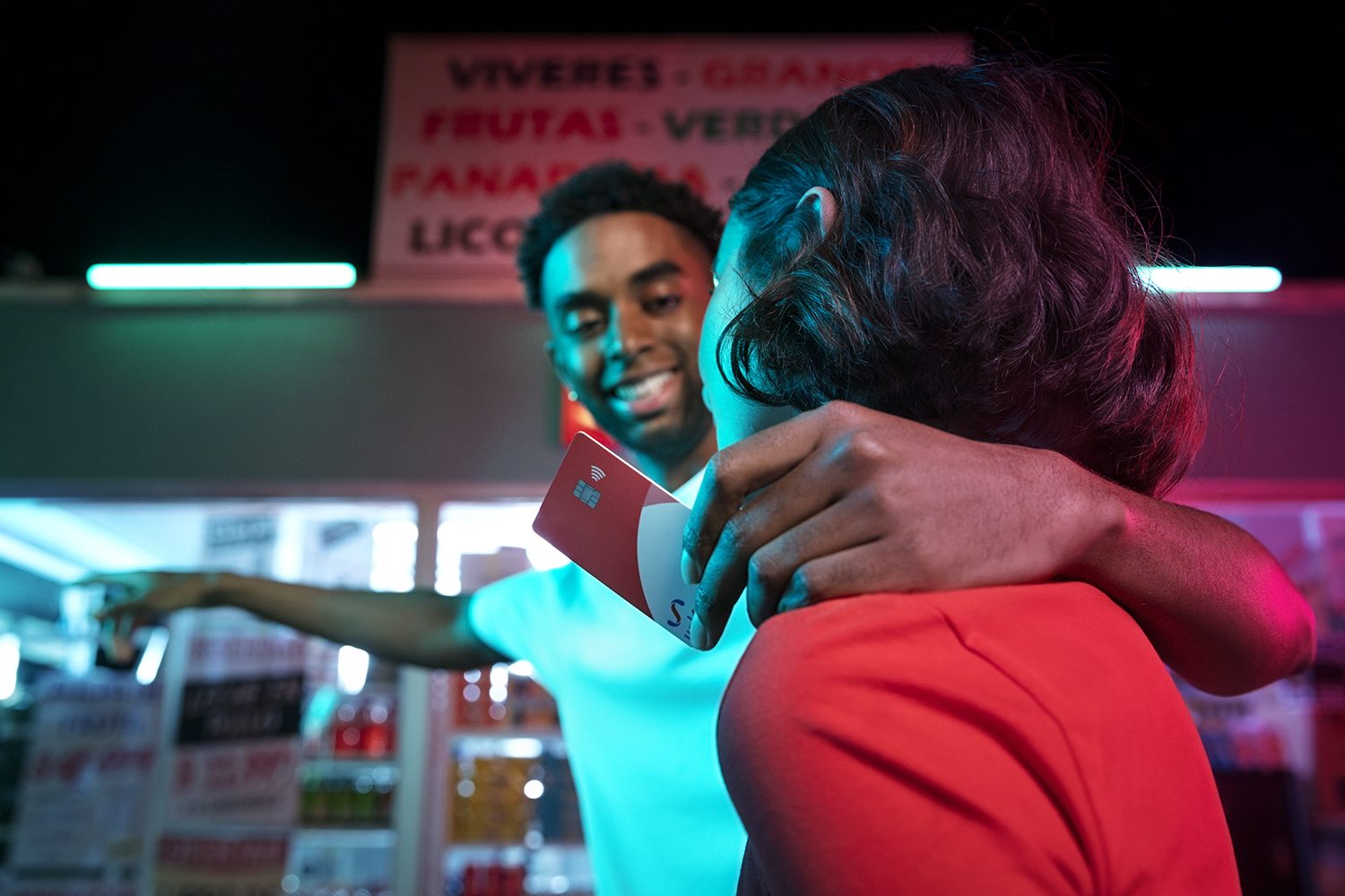Two people embrace outside a neon-lit corner shop