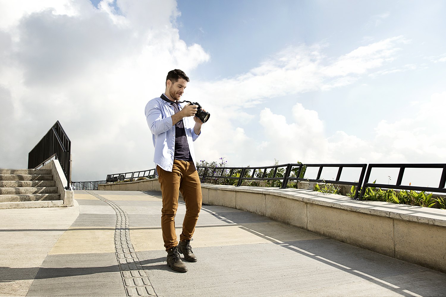 A man photographs from a wide concrete terrace above Medellín under a big cloud sky