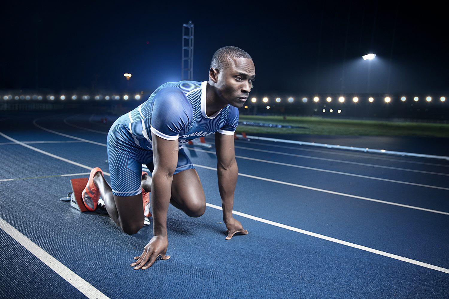 A sprinter in the starting blocks on a blue track