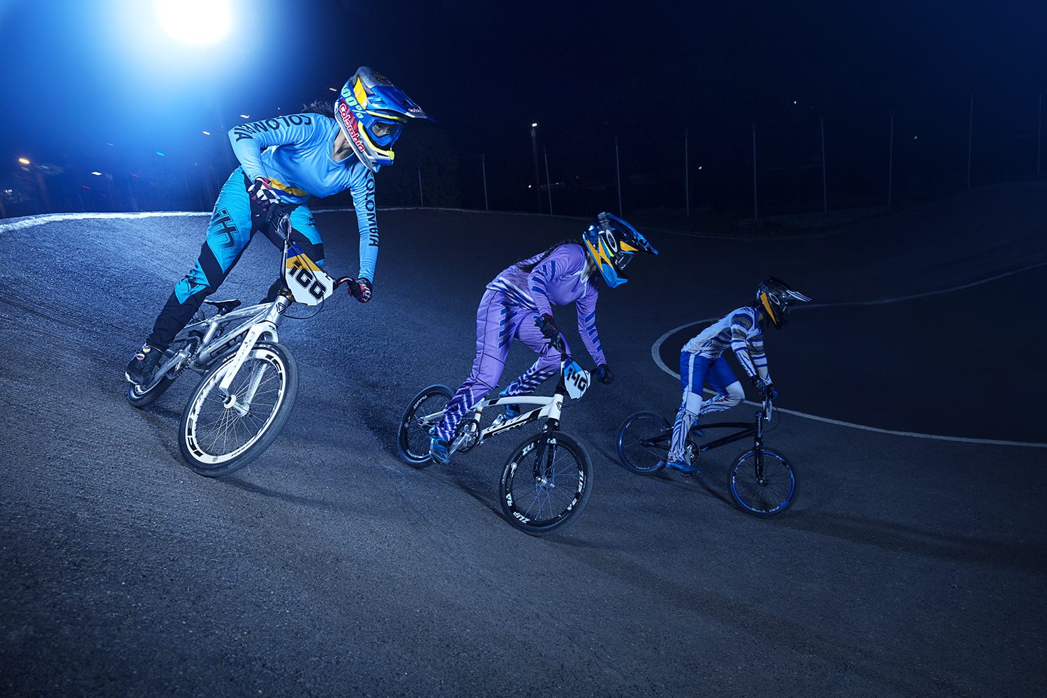 Three BMX riders poised under the lights