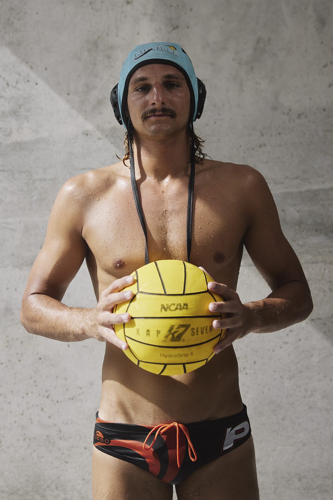 A player holds the ball to his chest, cap on, against a wall