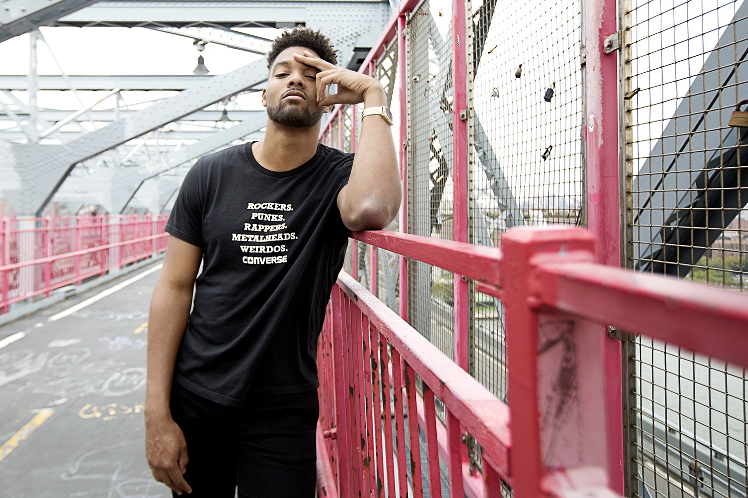 Walking the bridge path in a printed tee, hand raised against the light