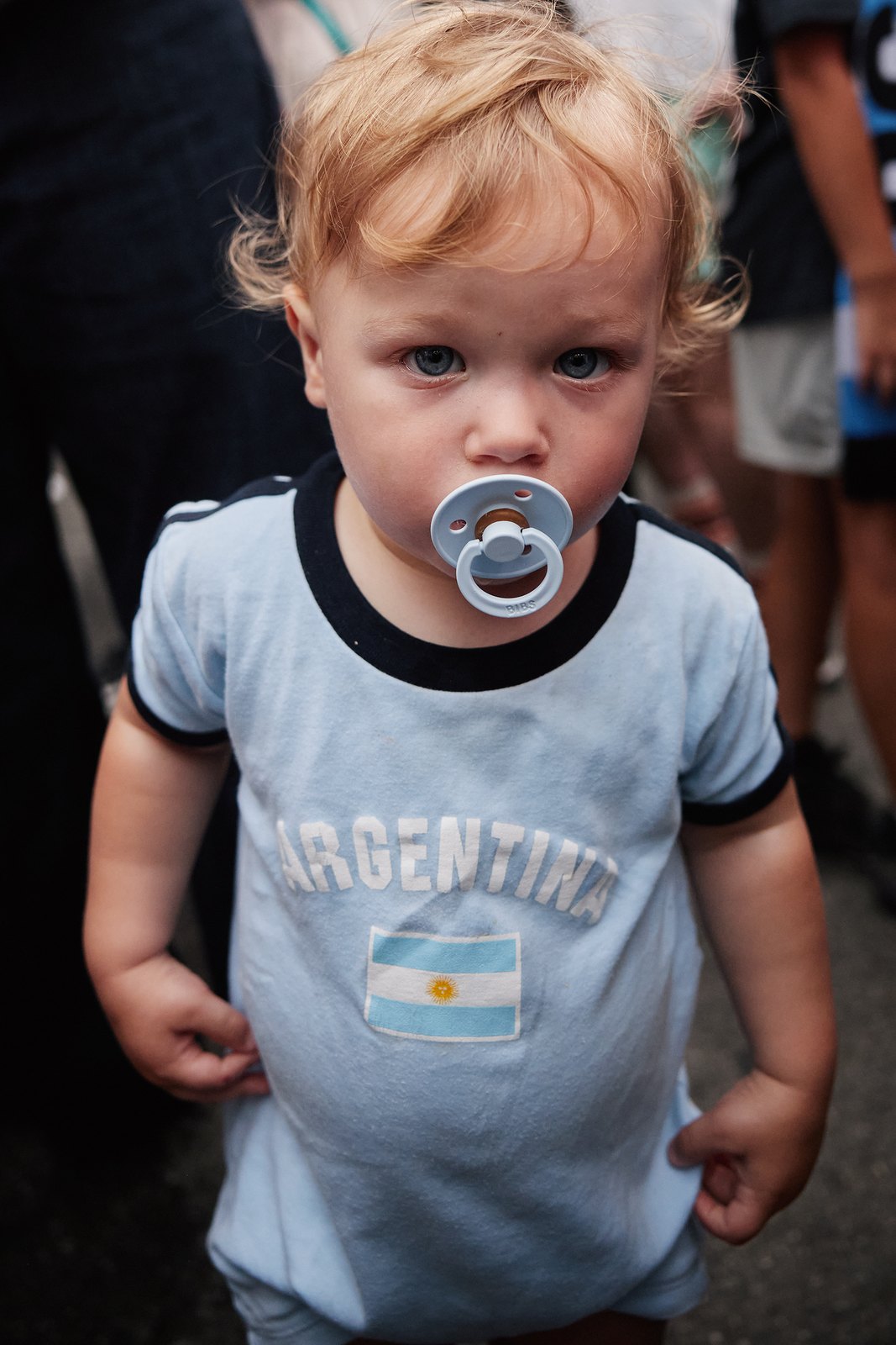 A small boy in an Argentina t-shirt with a pacifier looks straight into the lens