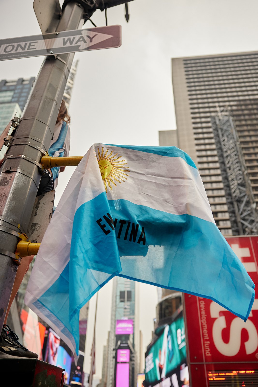 An Argentina flag flying beneath a New York ONE WAY sign, skyscrapers rising behind
