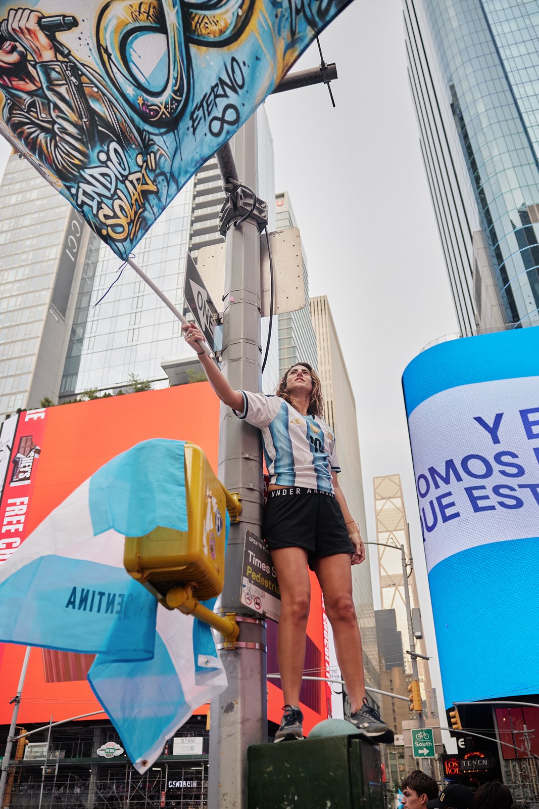 A supporter stands high above the crowd waving an enormous Argentina flag across Times Square