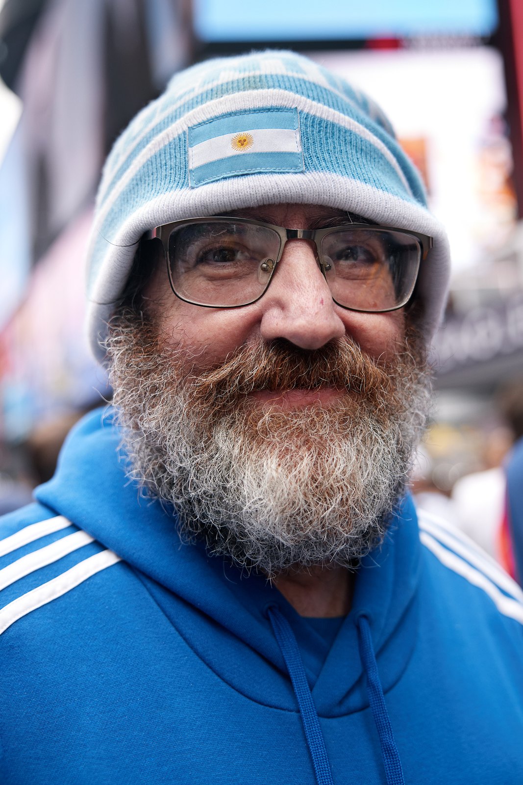 Portrait of an older bearded fan in an Argentina bucket hat, screens reflecting in his glasses